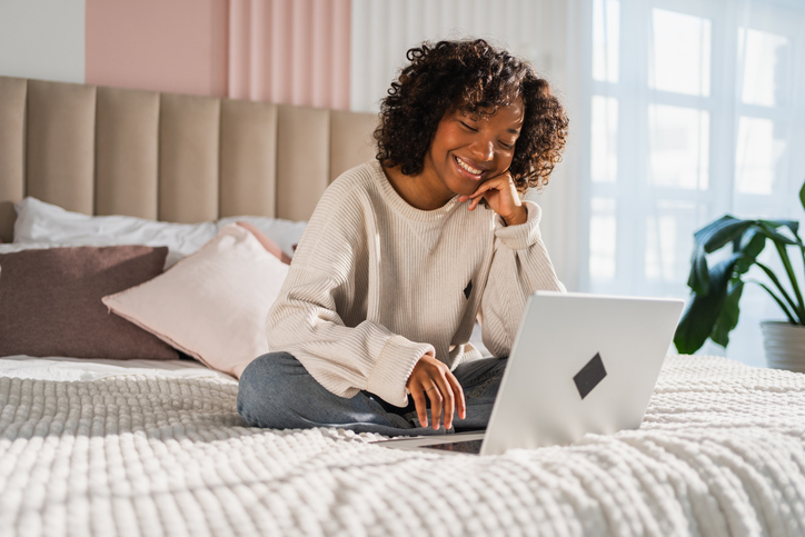a day in my dream life chatgpt - African American girl using laptop in bed at home office typing chatting reading writing email. Young black woman having virtual meeting online chat video call conference. Work learning from home.