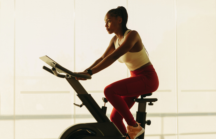 Healthy home workout: Sporty black female exercising on stationary bike