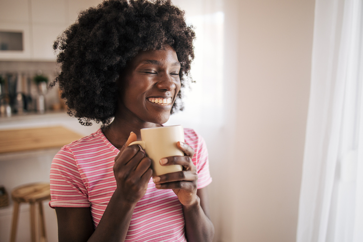 Happy African American woman drinking a cup of coffee at home and smiling
