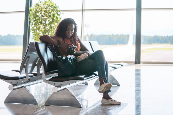 5 Best U.S. Cities To Travel Alone - Lovely Hispanic Adult Female Using Smartphone At The Airport