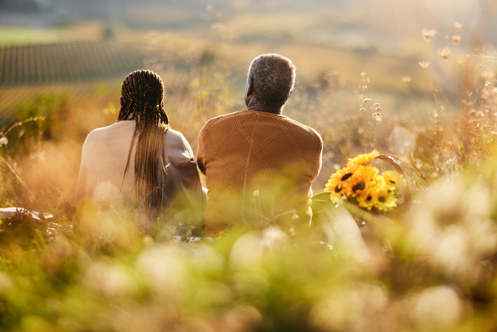Back view of black senior couple relaxing on a picnic on a hill.