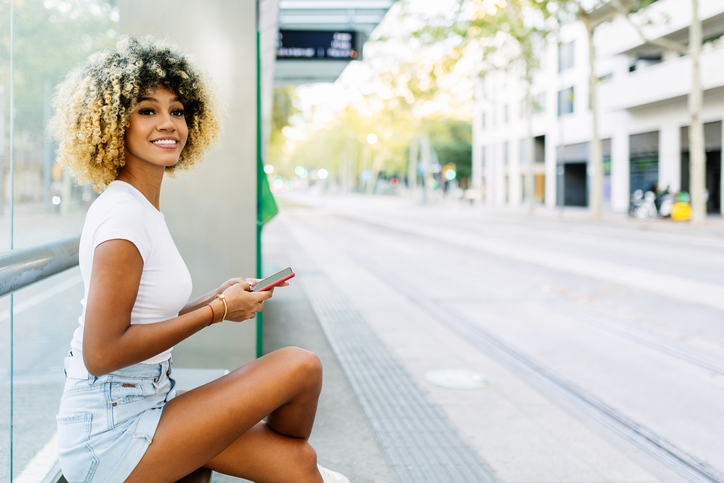 waiting seasons - Young beautiful Latin woman using smart mobile phone while waiting for the tram at stop station.