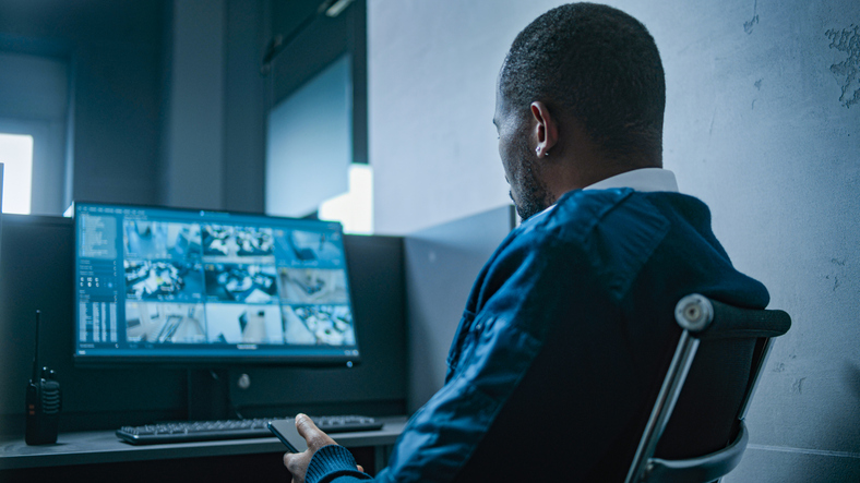 Male security guard uses mobile phone. Surveillance cameras on computer monitor