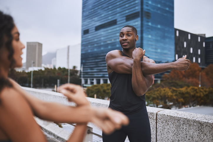 Young muscular man doing warm-up exercise with female friend on building terrace