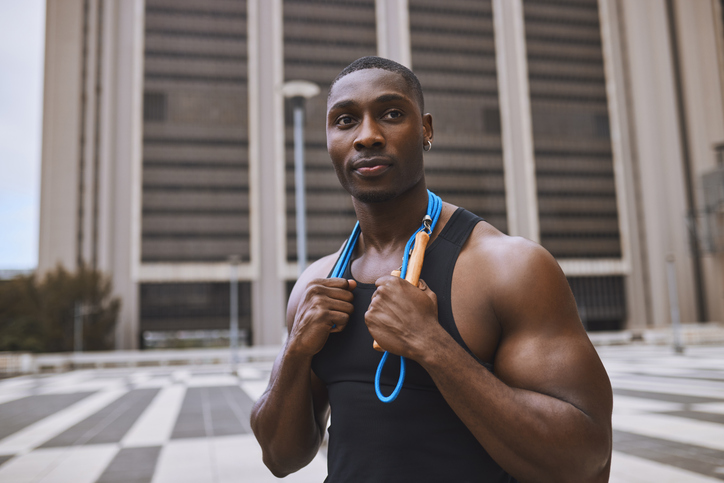 Close-up of young athletic man hanging jump rope around neck, looking proudly into distance outdoors