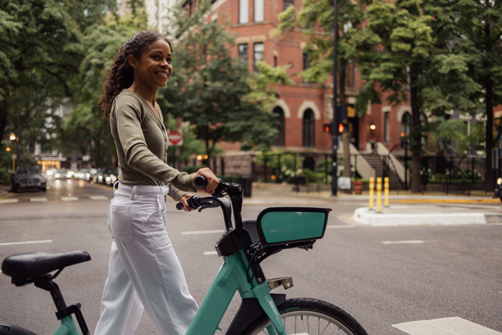 Happy African American woman walking with a bike on the street.