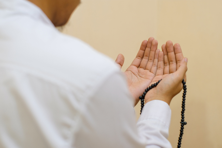 What Is an Imam - Close up Rear view hand of religious muslim man in white koko shirt with skullcap praying earnestly with his hands raised, holding islamic beads