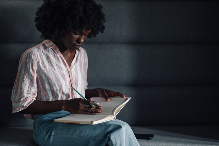 Bible Verses for Grief - Focused diverse casual employee writing down in textbook at office.