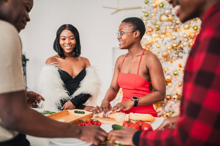 Hosting Tips for Friendsgiving - Thanksgiving Day / Christmas preparations. African American friends preparing meals and setting the table.