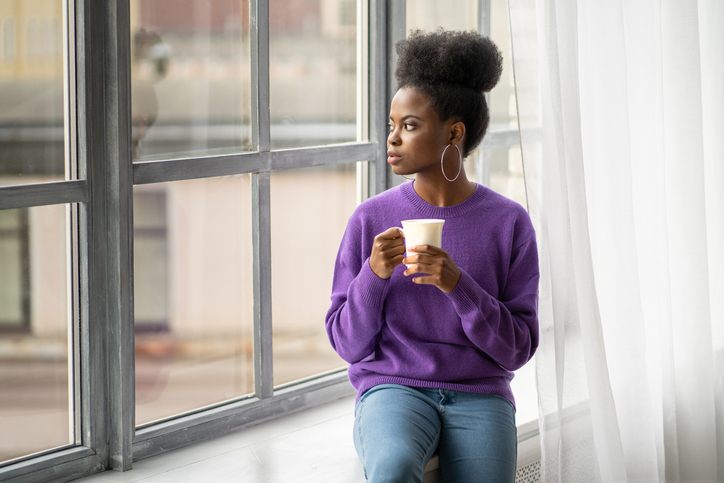 Young Woman Holding Coffee Cup Standing By Window