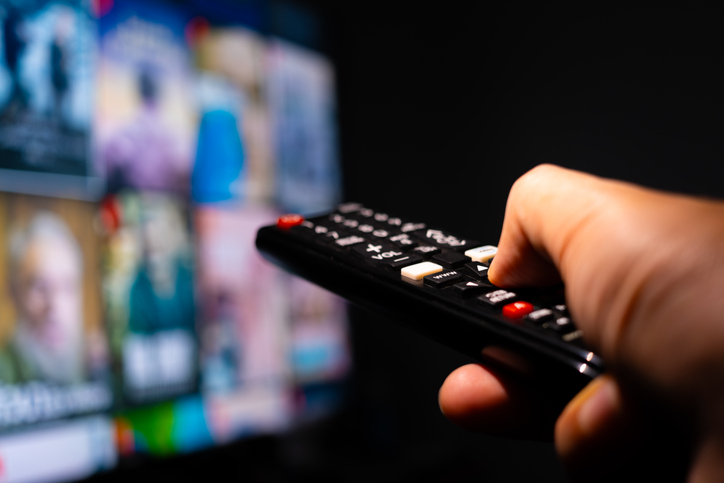 netflix changes - Man's hand holding a remote control, multimedia, online TV, broadcasting entertainment to viewers at home. The idea behind the broadcast