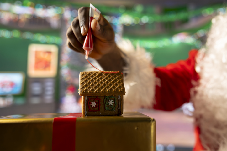 mental health holidays with family - Santa Claus adds icing on homemade cookies to create a gingerbread house