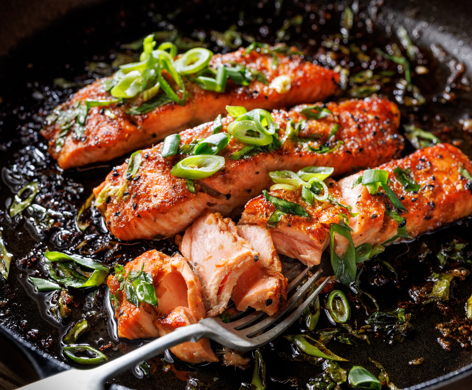 Close-up view of teriyaki salmon sprinkled with chopped scallion in a black baking dish