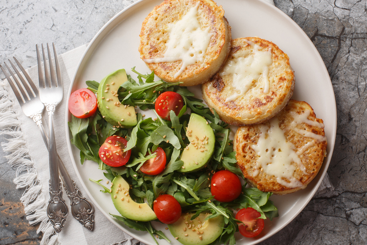 Fried crumpets in beaten egg with fresh vegetable salad for breakfast close-up in plate. Horizontal top view