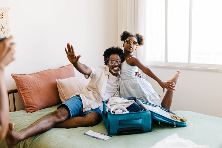 Excited father and daughter posing for mom's camera while packing for a vacation
