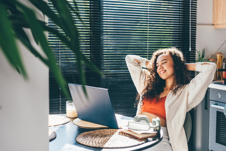 holistic self-care - Young woman with laptop relaxes while working in the kitchen.