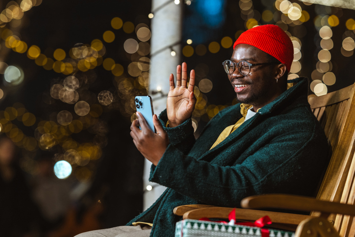 Smiling man enjoying holiday video call outdoors with festive lights