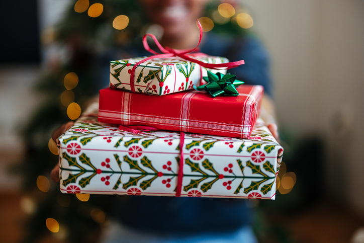 Festive Christmas Gifts Held by a Person Near a Decorated Tree