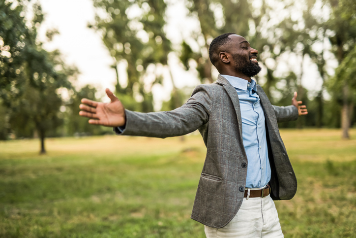 Black businessman standing with arms open in nature