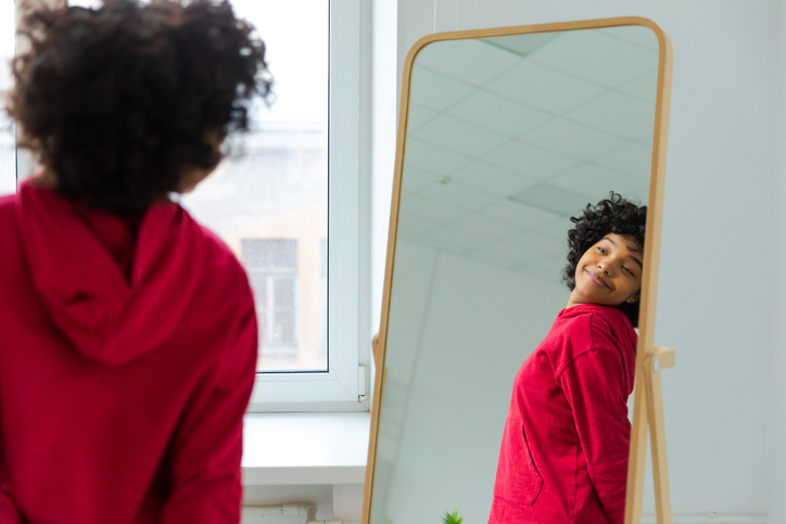 Love yourself. Beautiful young smiling african american woman dancing enjoying her mirror reflection. Black lady looking at mirror looking confident and happy. Self love concept.