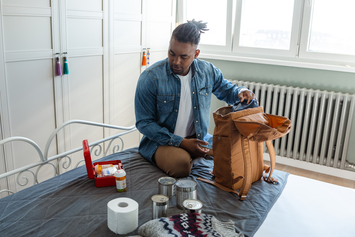 African American young man preparing emergency supplies on bed at home