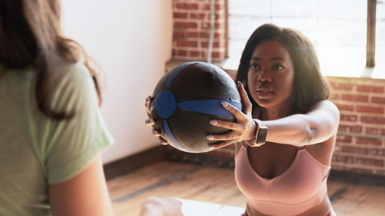 A black woman exercises with a medicine ball in a gym.