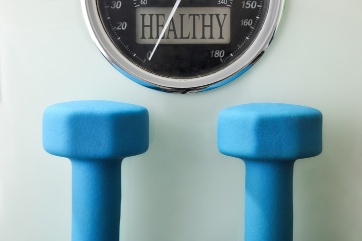 Two blue neoprene dumbbells on scale with health message