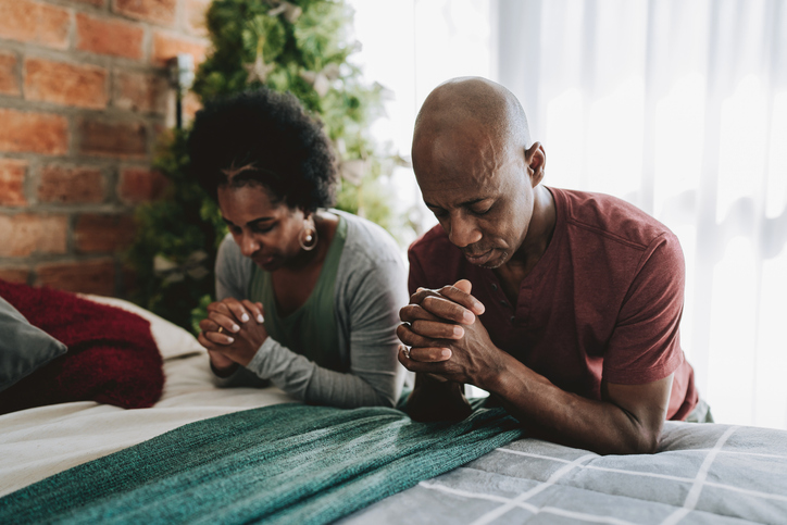 Couple praying kneeling on the bed in the bedroom