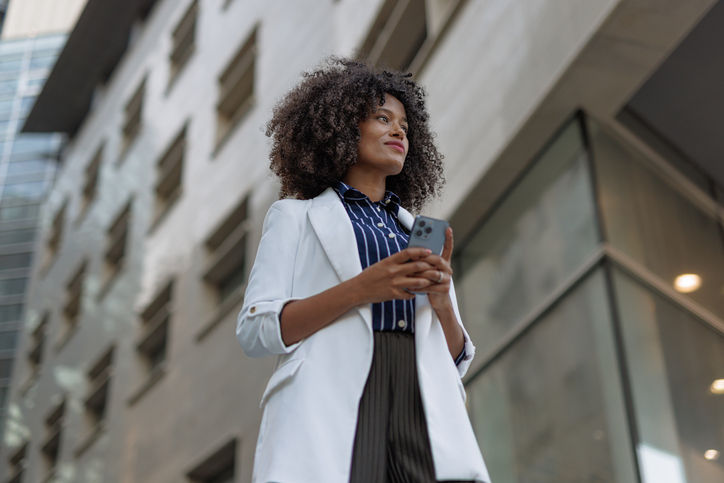 Happy young business woman using a smartphone on her way to the office