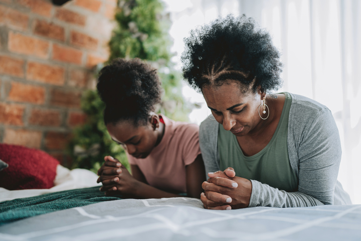 Mother and daughter praying on their knees in their bedroom
