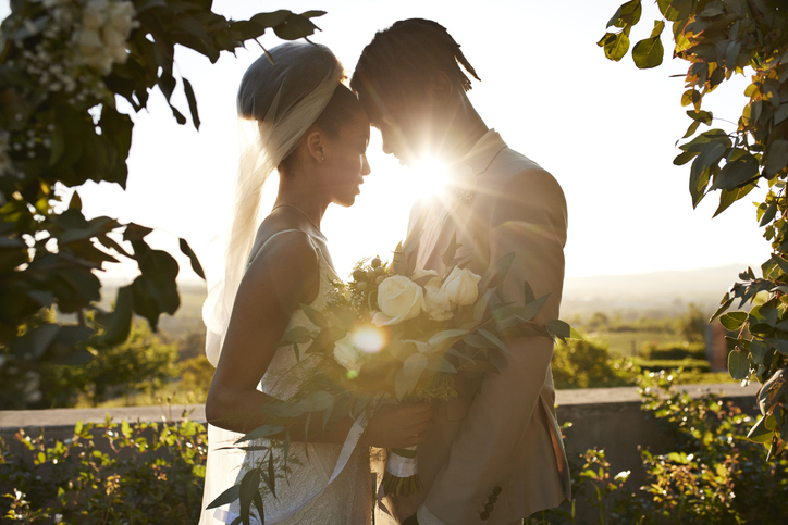 Back lit bride and groom touching foreheads at wedding altar