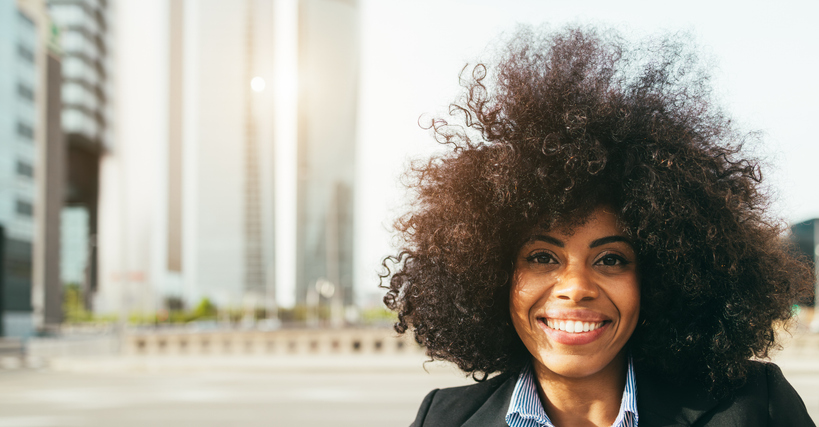 African american business woman smiling on camera with city skyscrapers in background - Entrepreneur and female career concept - Focus on face