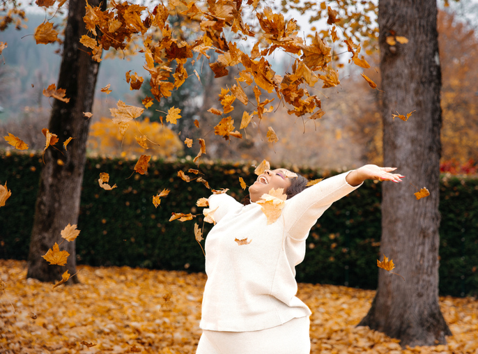 Caucasian mature female enjoying autumn leaves in a park with joyful expression
