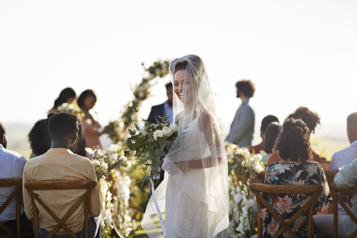 Cheerful bride with bouquet standing at aisle near guests