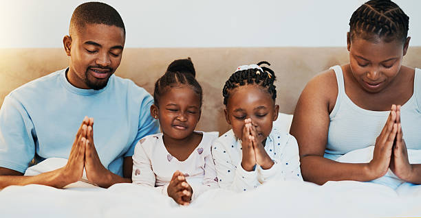 Worship, support and prayer with black family in bed for trust, spiritual and morning bonding. Love, God and christian faith with parents and children at home for religion, gratitude and catholic